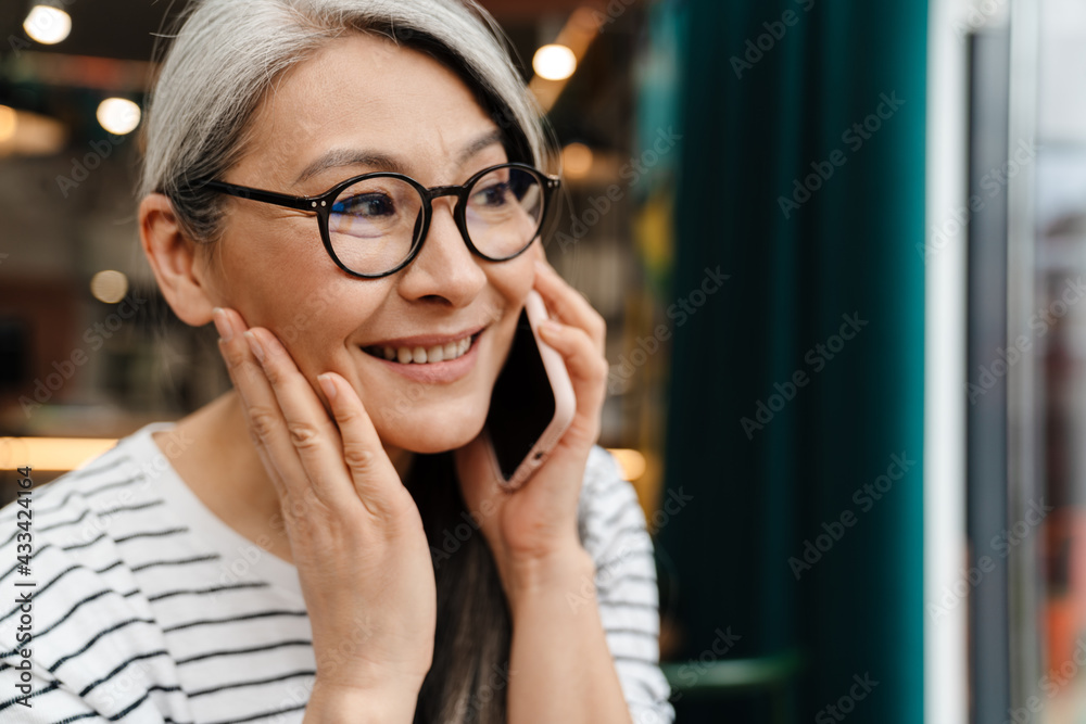 Mature woman smiling and talking on cellphone in cafe indoors Mature woman smiling and talking on cellphone in cafe indoors