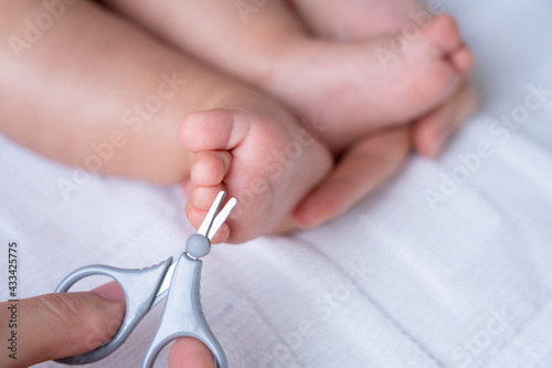 The hands of a mother with scissors make a pedicure for a newborn child.