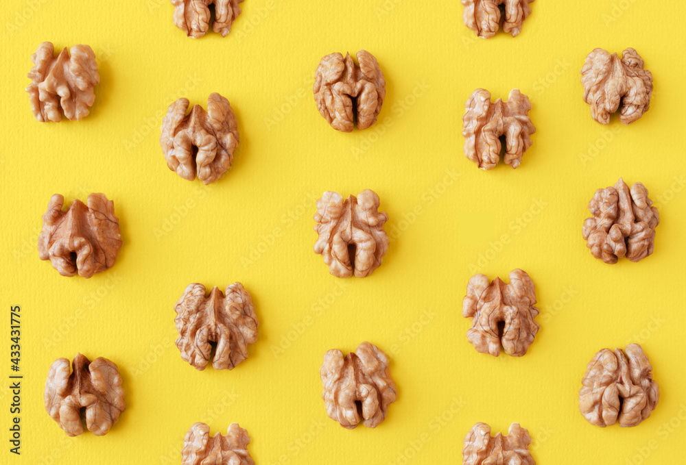 Obraz premium Halves of walnuts on a yellow trendy color 2021 year background, pattern, top view.