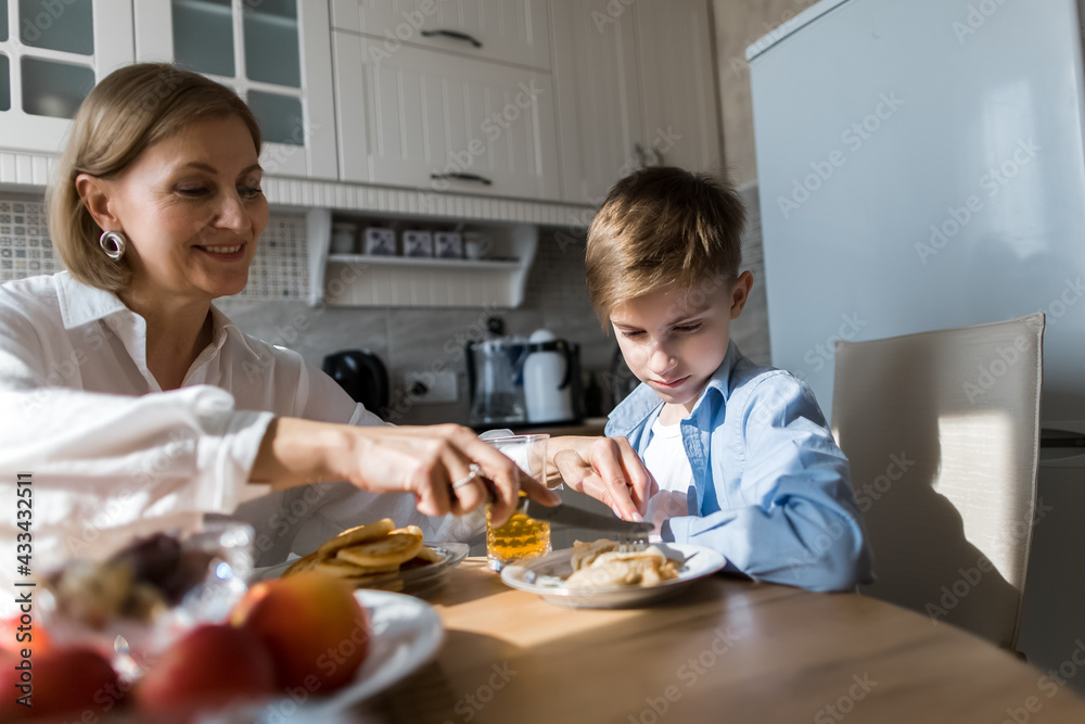 Adult woman in the kitchen treats a child with pancakes and juice. Adult woman in the kitchen treats a child with pancakes and juice.