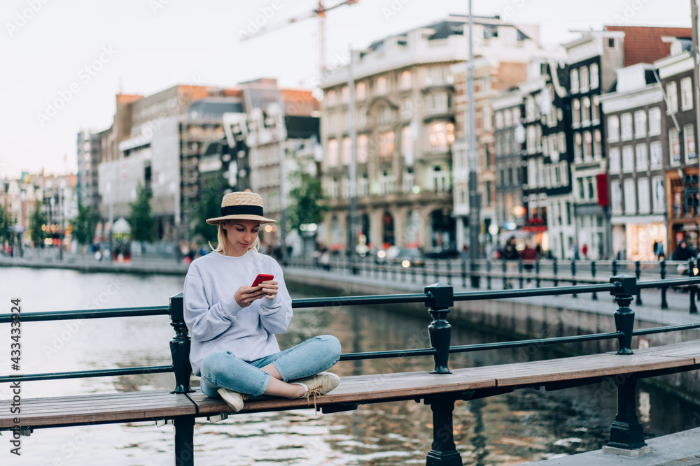 Stylish female tourist using smartphone near canal in historic district on bridge