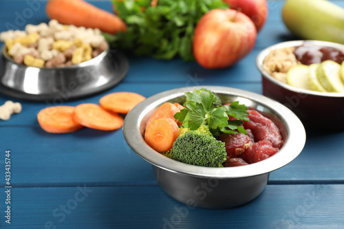 Natural pet food in feeding bowls on blue wooden table, closeup
