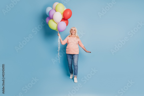 Photo of pensioner dreamy woman hold many air baloons in pink sweater on blue background