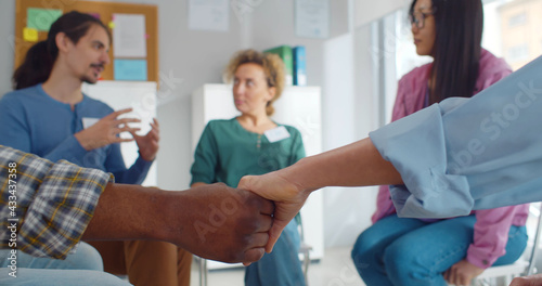 Close up of african and caucasian people holding hands sitting in circle during therapy session in support group