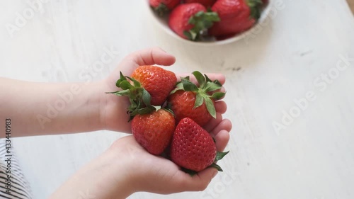 Children's hands hold ripe juicy strawberries on a white wooden background. The concept of healthy food, organic food and beverages.
