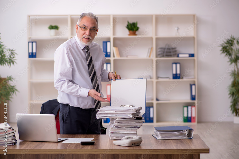 Aged male employee unhappy with excessive work in the office Aged male employee unhappy with excessive work in the office