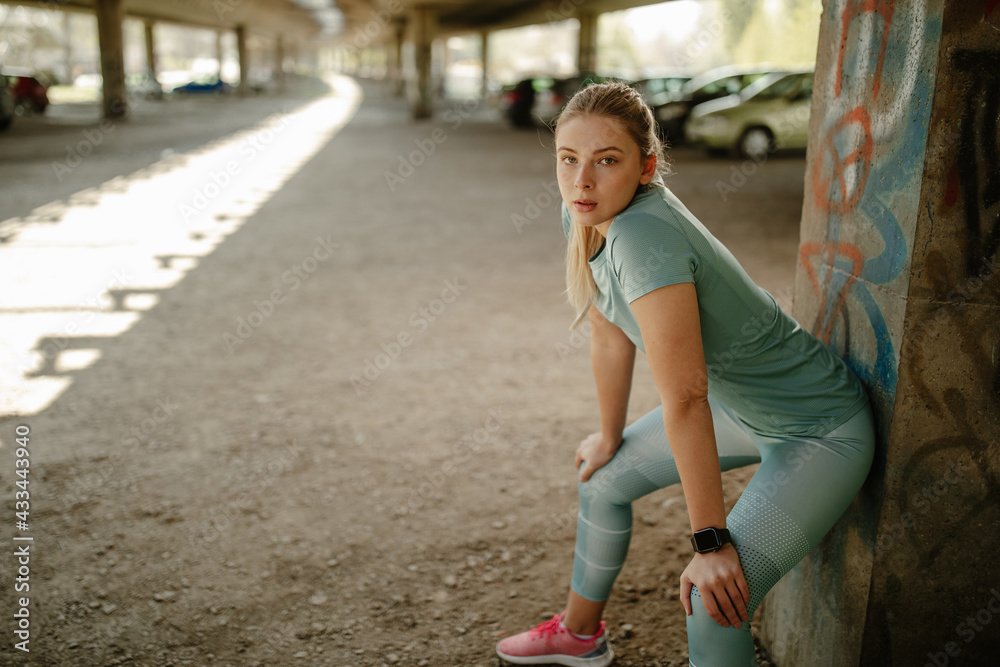 woman wearing sports wear leaning a wall looking at camera. Fitness female taking a break.