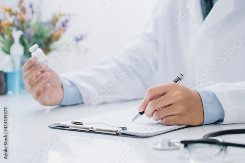 Doctor holding prescription bottle and writing prescription on special form at office room. Healthcare, Vaccine,medical and pharmacy concept.