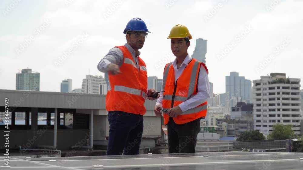Solar power plant engineer manager with walkie talkie talking to asian worker control inspecting photovoltaic on rooftop in urban city. technician checking Solar Cell on roof outdoors on cityscape Solar power plant engineer manager with walkie talkie talking to asian worker control inspecting photovoltaic on rooftop in urban city. technician checking Solar Cell on roof outdoors on cityscape