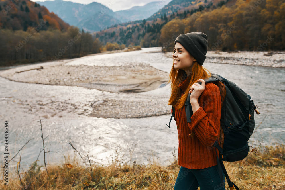 woman in a red sweater and cap with a backpack on her back in the mountains near the river in nature