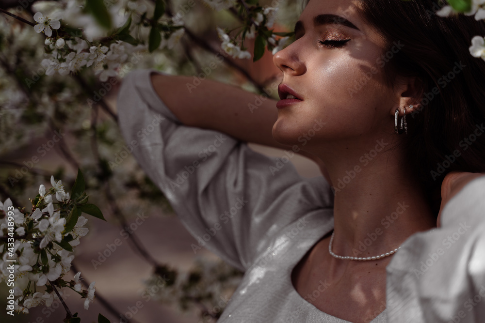 The sun shines on the girl's face near the flowering trees in the park. Portrait of attractive girl with curly hair in the garden. The sun shines on the girl's face near the flowering trees in the park. Portrait of attractive girl with curly hair in the garden.