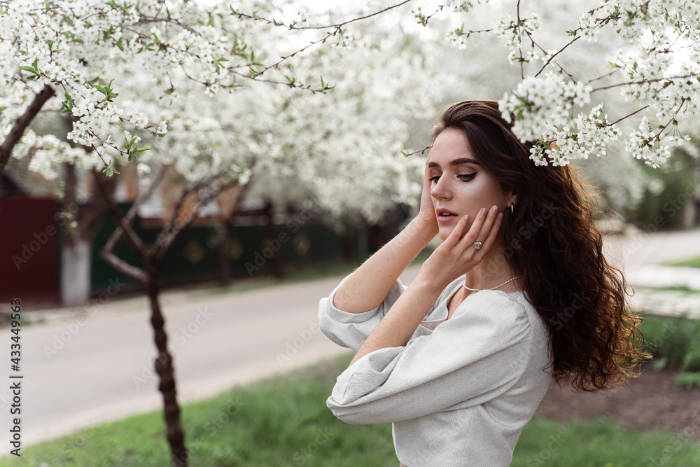 Spring lifestyle. Model posing near white blooming trees without mask outdoor countryside. Dreaming girl with curly hair. Spring lifestyle. Model posing near white blooming trees without mask outdoor countryside. Dreaming girl with curly hair.