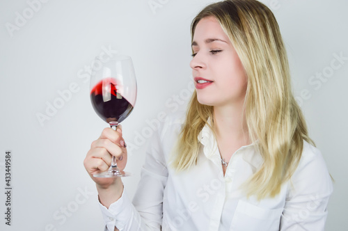 Portrait of a beautiful young blonde woman swirling the red wine in the glass to aerate the wine and release its bouquet at a wine tasting
