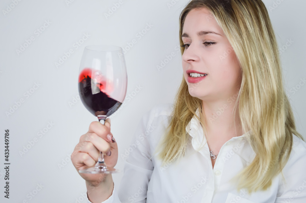 Portrait of a beautiful young blonde woman swirling the red wine in the glass to aerate the wine and release its bouquet at a wine tasting Portrait of a beautiful young blonde woman swirling the red wine in the glass to aerate the wine and release its bouquet at a wine tasting