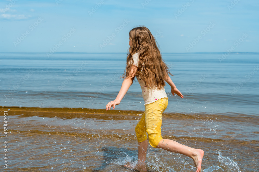 A little girl in bright yellow pants runs in the water and frolics on the beach A little girl in bright yellow pants runs in the water and frolics on the beach