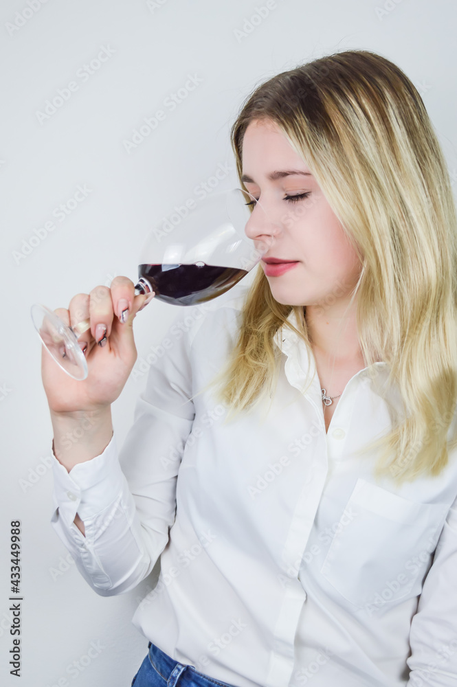 Portrait of a beautiful young blond woman sniffing red wine in the glass to feel its bouquet at a wine tasting Portrait of a beautiful young blond woman sniffing red wine in the glass to feel its bouquet at a wine tasting