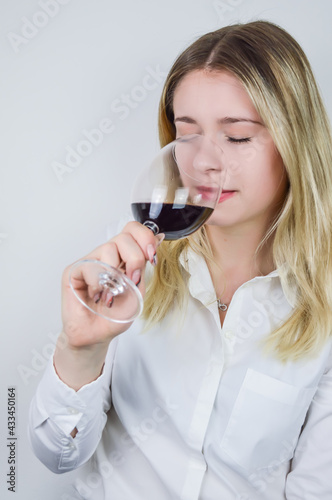 Portrait of a beautiful young blond woman sniffing red wine in the glass to feel its bouquet at a wine tasting
