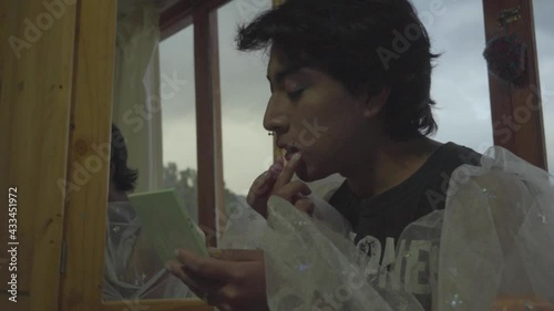 Joven queer retocándose los labios frente a su espejo de mano 