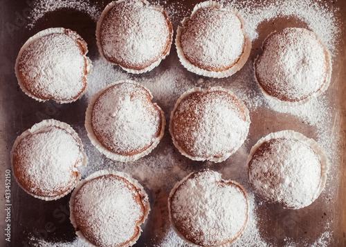 Close-up of muffins on a tray. Powdered sugar cakes. The work of the confectionery industry. Each cupcake is wrapped in paper wrapping.