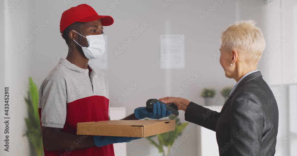 Obraz premium Deliveryman in safety mask and gloves delivering pizza box to mature businesswoman in office