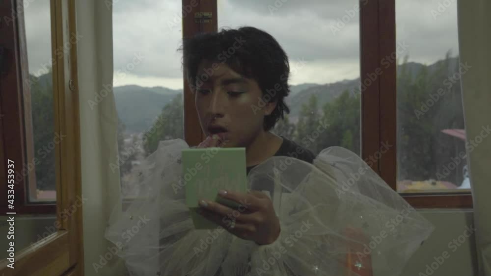 Joven queer maquillado pintándose los labios en su habitación 