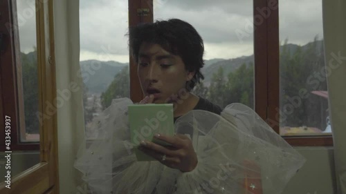 Joven queer maquillado pintándose los labios en su habitación 