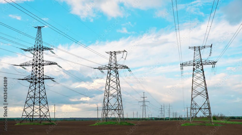 High voltage lines and power pylons in a flat and agricultural landscape on a sunny day with clouds in the blue sky.