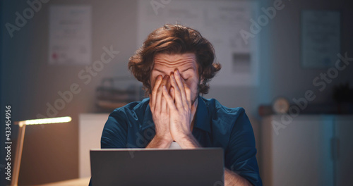 Young businessman having headache working overtime with laptop at office late night. photo