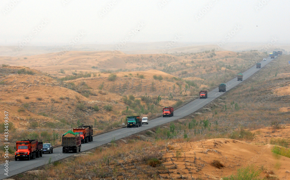 Freight trucks are running on a road in the desert of Kubuchi, China.