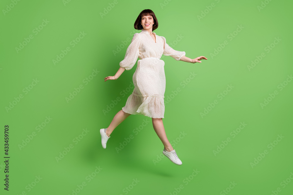 Full length body size photo woman wearing dotted dress jumping up running smiling isolated pastel green color background Full length body size photo woman wearing dotted dress jumping up running smiling isolated pastel green color background
