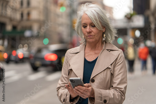 Mature caucasian woman in city walking street using cellhpone