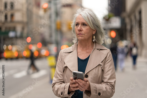 Mature caucasian woman in city walking street using cellhpone