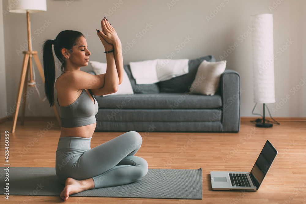Young woman practicing yoga online via laptop at home