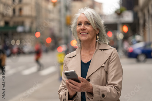 Mature caucasian woman in city walking street using cellhpone