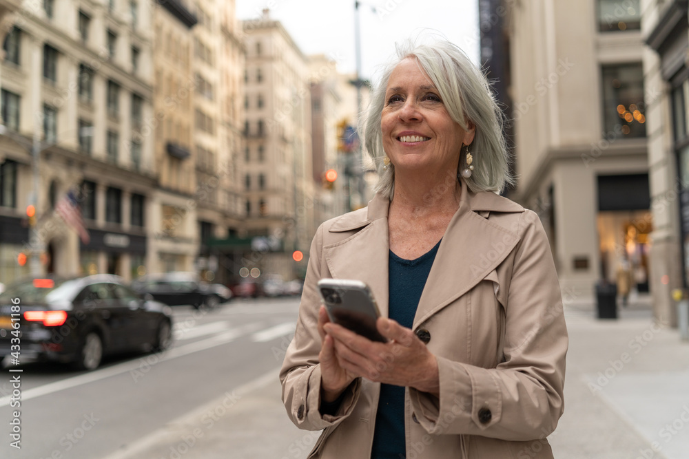 Mature caucasian woman in city walking street using cellhpone