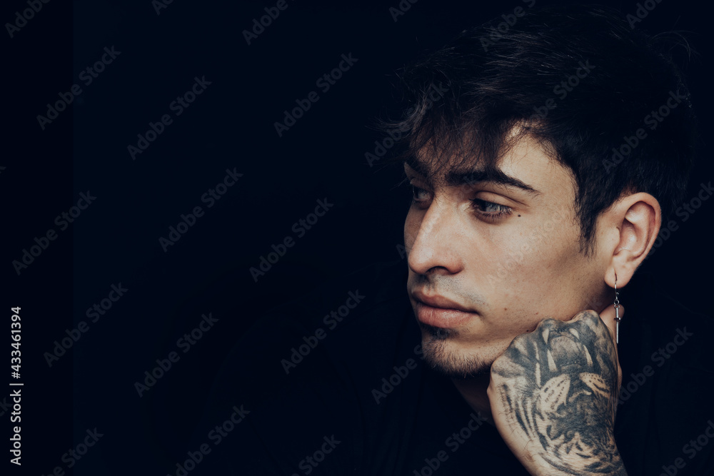 Young man with tattoos and earrings looking aside with a pensive expression