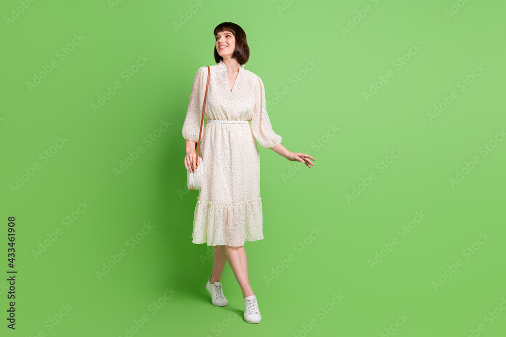 Full length body size photo smiling woman going wearing dotted dress looking empty space isolated pastel green color background Full length body size photo smiling woman going wearing dotted dress looking empty space isolated pastel green color background