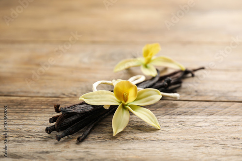 Beautiful vanilla flowers and sticks on wooden table  closeup