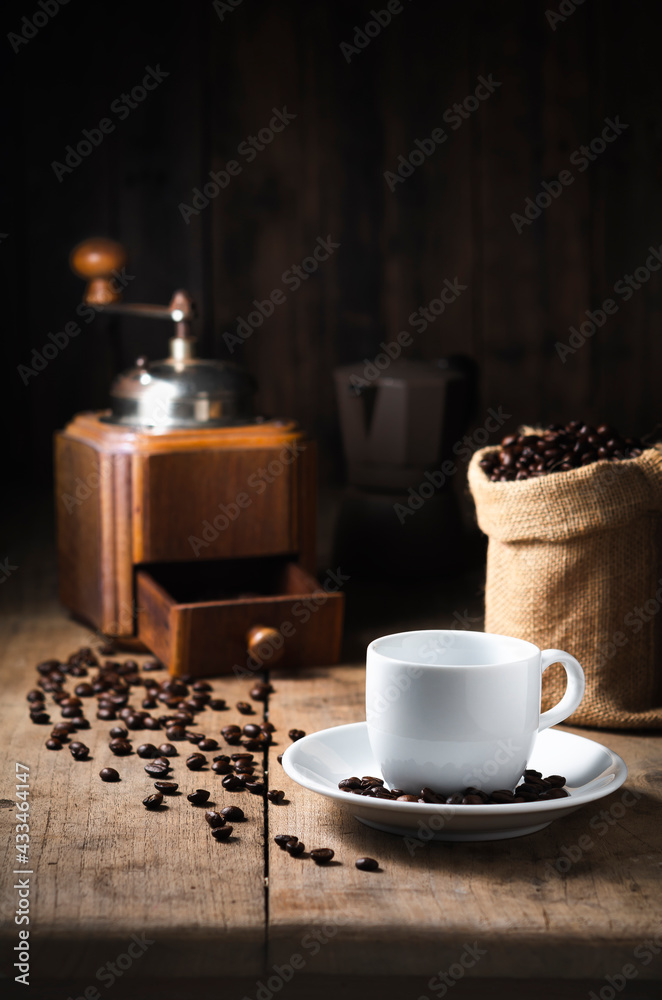 The white coffee cup on the dish. top the old wood table has coffee vintage grinder beans and Moka pot as dark tone background the Top copy space The white coffee cup on the dish. top the old wood table has coffee vintage grinder beans and Moka pot as dark tone background the Top copy space
