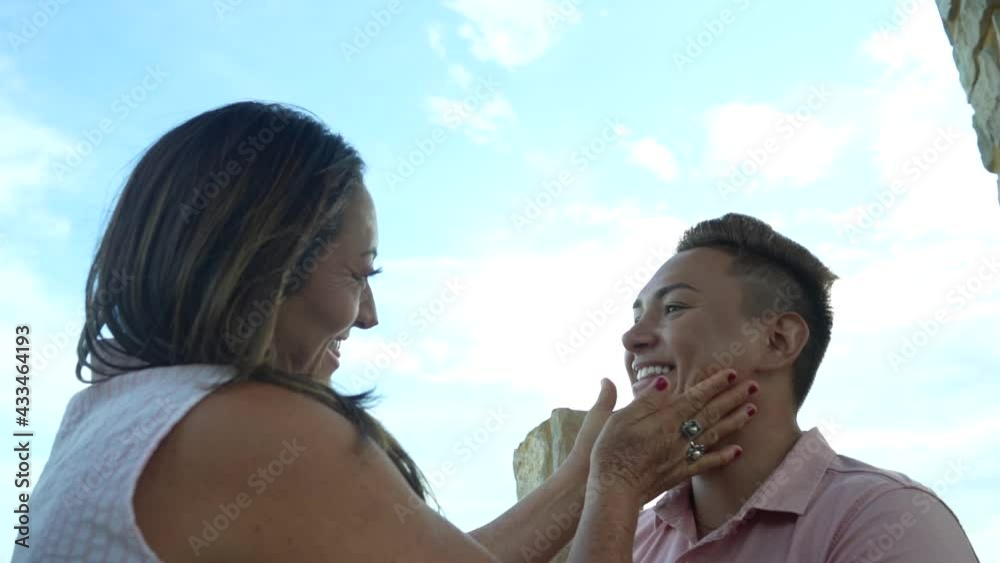 Madre acariciando con las manos el rostro a su hijo gay con el cielo de fondo 