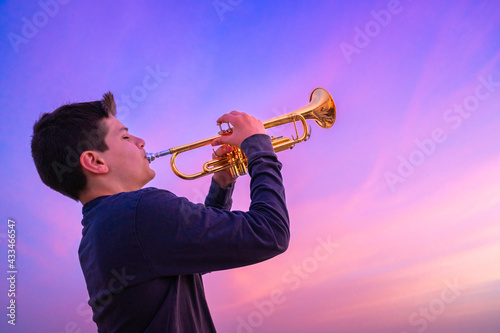 Teen boy playing trumpet against a beautiful sunset sky