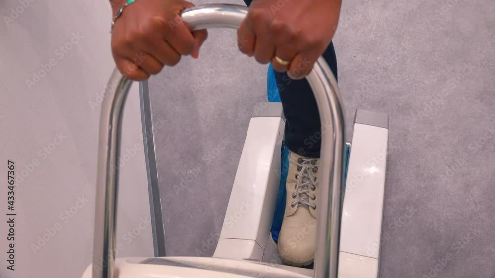 The client pulls on shoe covers before entering a clean medical facility. Using a special tool. Hands hold the sound of the handle.