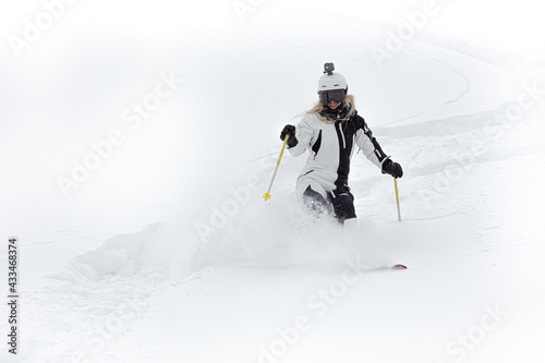 happy girl in black and white overalls beautifully rides downhill skiing in a helmet with an action camera on her head. young woman freeriding - super ski photo for advertising and publications