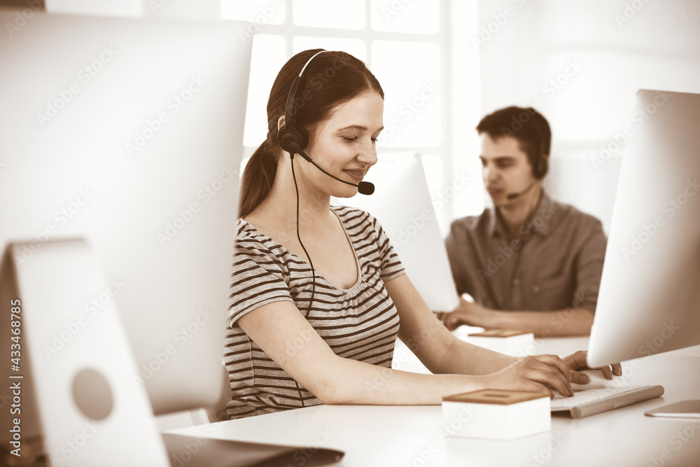 Casual dressed young woman using headset and computer while talking with customers online. Group of operators at work. Call center, business concept Casual dressed young woman using headset and computer while talking with customers online. Group of operators at work. Call center, business concept
