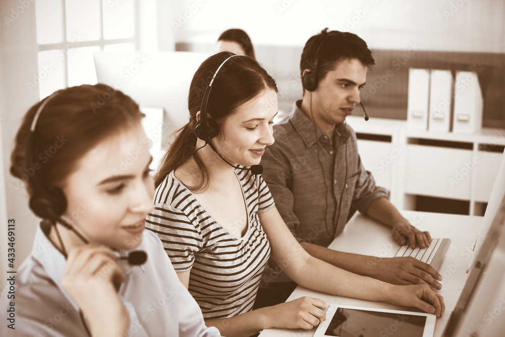 Casual dressed young woman using headset and computer while talking with customers online. Group of operators at work. Call center, business concept Casual dressed young woman using headset and computer while talking with customers online. Group of operators at work. Call center, business concept