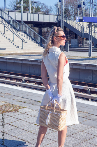 beautiful blonde woman in her 40s in white dress standing at train station