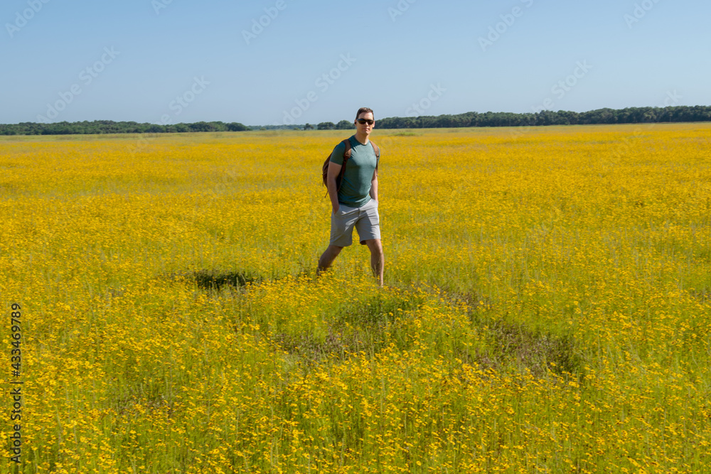 Handsome Healthy Young Man With Backpack Hiking Through Field of Yellow Wild Flowers