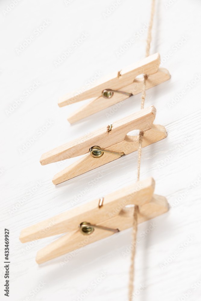 three wooden clothespins with a metal spring hang on a rope on a white background. selective focus