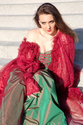 beautiful brunette woman in red evening dress sitting outside on stairs in the sun