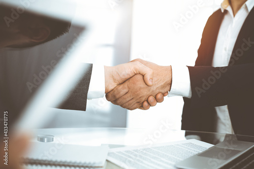 Unknown diverse business people are shaking hands finishing contract signing in sunny office, close-up. Business handshake concept